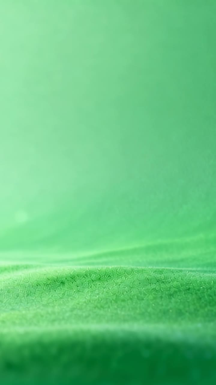Vídeo vertical: Fundo verde texturizado se acomodando, mostrando pequenas mudanças de luz nas dobras de uma mesa de estúdio.