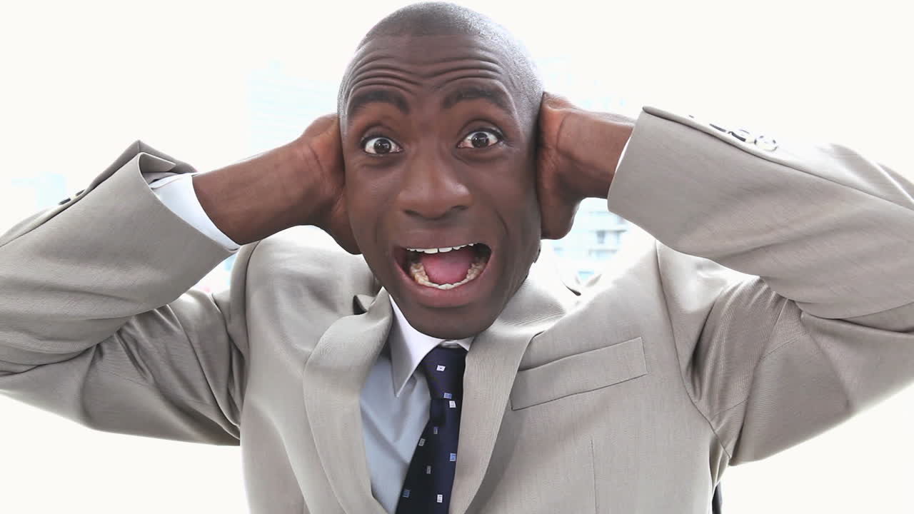 un homme d'affaires noir criant les mains sur ses oreilles.