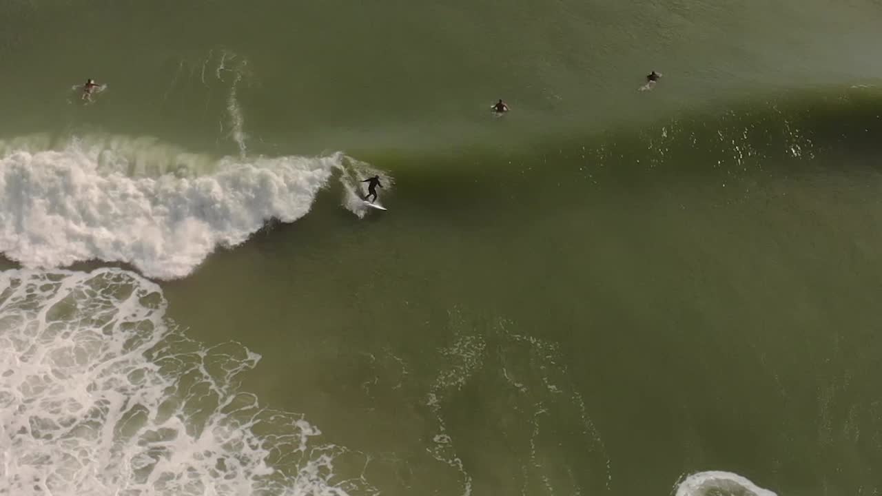 Sorvolo aereo di surfisti che cavalcano le onde lungo la costa