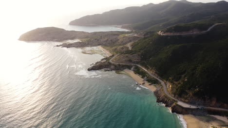 Aerial-view-showing-tropical-coastline-of-Vinh-Hy,-Nui-Chua-in-Vietnam-with-mountains,-road,sandy-beach-and-ocean-during-sunset