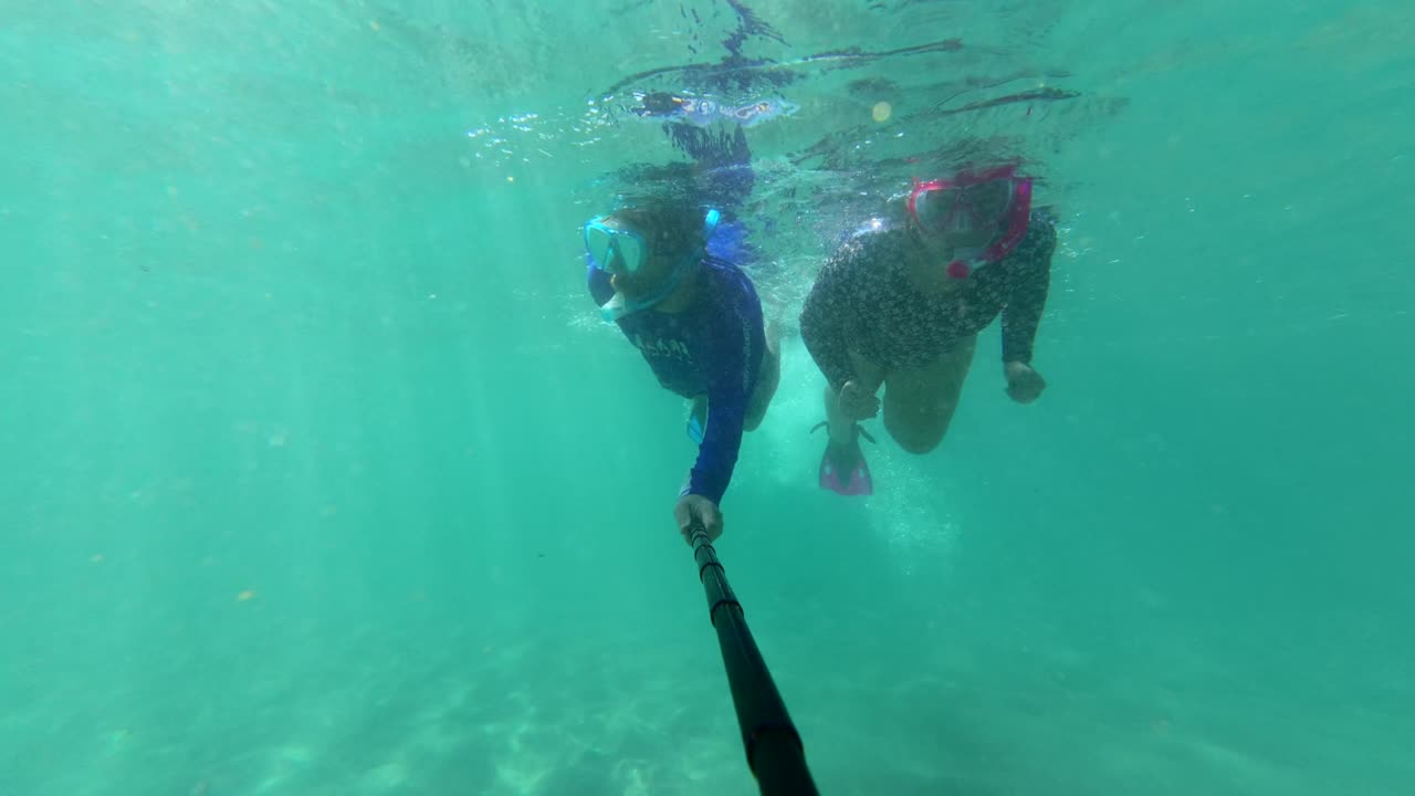 Un hombre y una mujer practicando esnórquel en aguas cristalinas, haciendo el signo de «OK» con la mano y saludando a la cámara cerca de la playa de La Morita, México