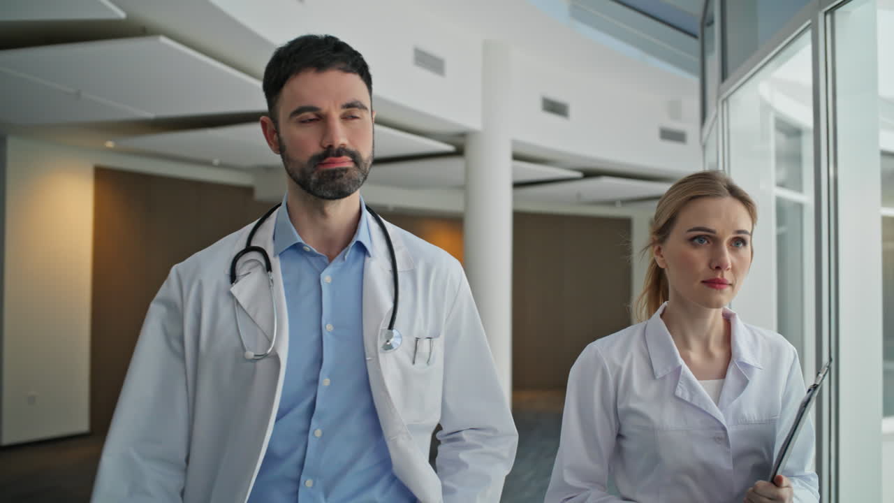 Beyaz önlükleriyle klinikte yürüyen başarılı doktorlar (yakın çekim). Ciddi sağlık personeli.