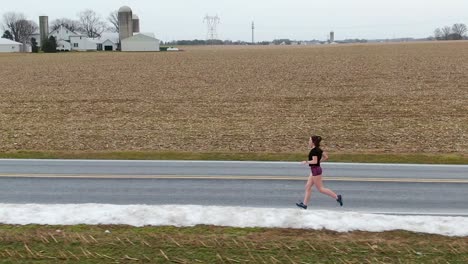 female runner in shorts training for race during winter among rural farmland in pennsylvania, usa.  copy space. determination, grit, fitness, cardiovascular exercise, health, female empowerment theme.