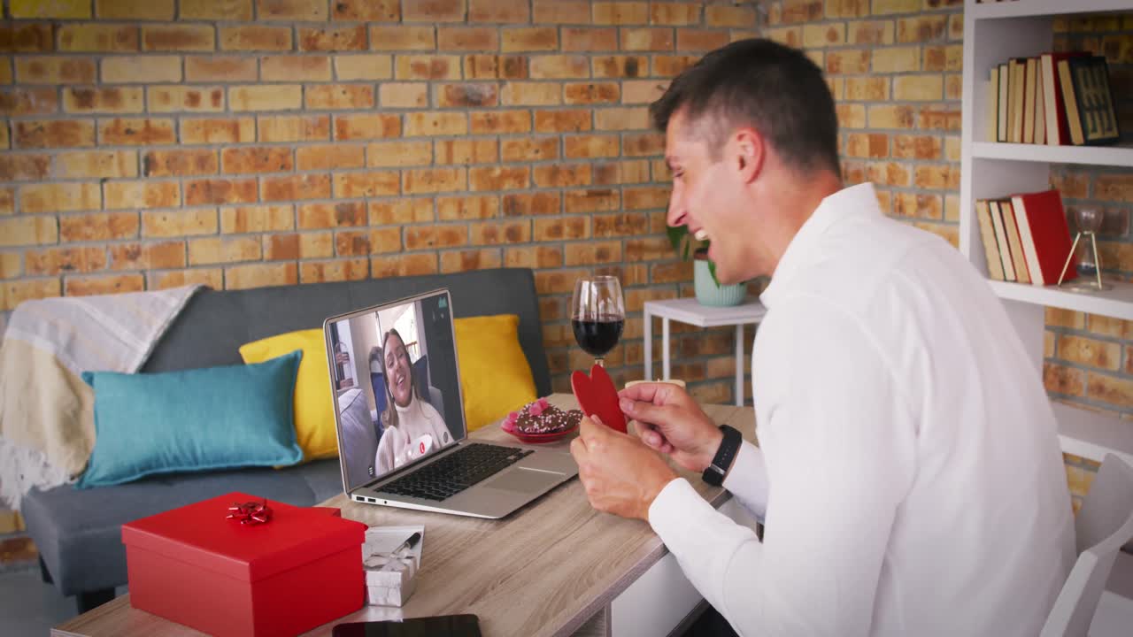 발렌타인 데이트에서 백인 커플 비디오 통화 노트북 화면에 미소 짓는 남자가 심장을 들고