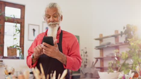 Half-face-of-happy-biracial-potter-with-long-beard-using-smartphone-in-pottery-studio,-slow-motion