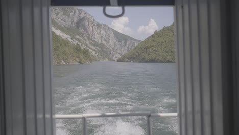 a ferry trip in albania from fierze to koman over the lake with a majestic nature around on a sunny day with clouds looking over the river seen from the back of the boat in between two walls log