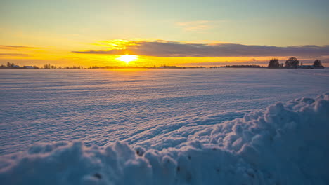 plano general de una puesta de sol dorada en el horizonte iluminando un paisaje blanco de invierno, time-lapse