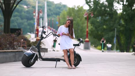 woman using phone on electric scooter in city park