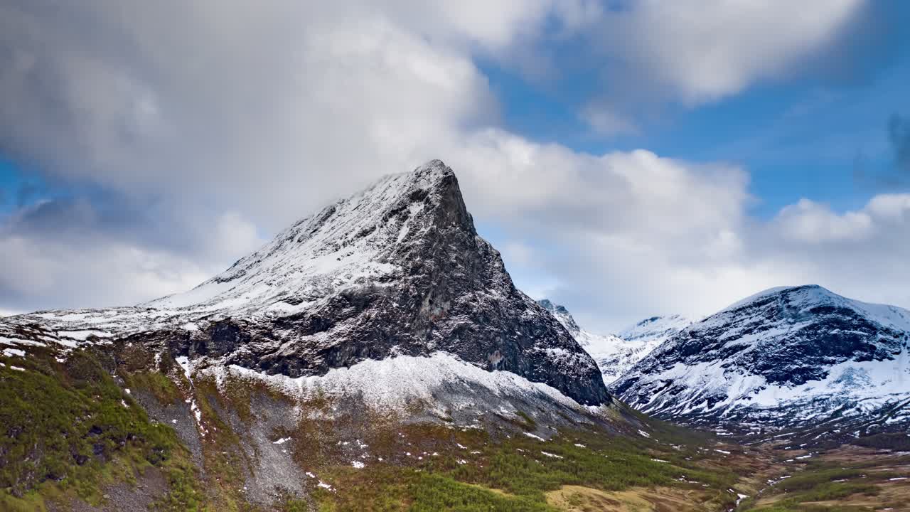 A lonely mount Hereggja soaring above the lush Herdalen valley. Farmland stretching up to the foothills of the mountain range. Green pastures under the bright blue sky and white clouds.