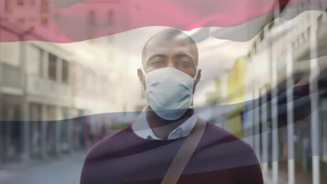 Animation-of-flag-of-netherlands-waving-over-man-wearing-face-mask-during-covid-19-pandemic