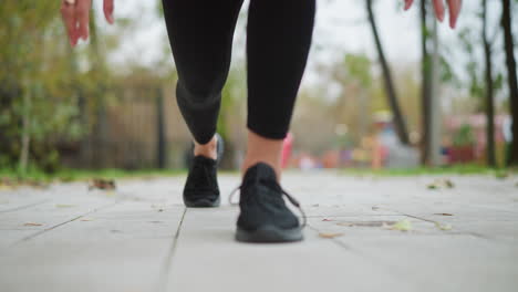 close view of lady s leg in black sneakers set on ground, ready to run with hands down in a game park, focused athletic action shot in a park setting, preparing for a run or exercise session