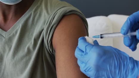 midsection of gloved female doctor giving vaccination to senior african american man