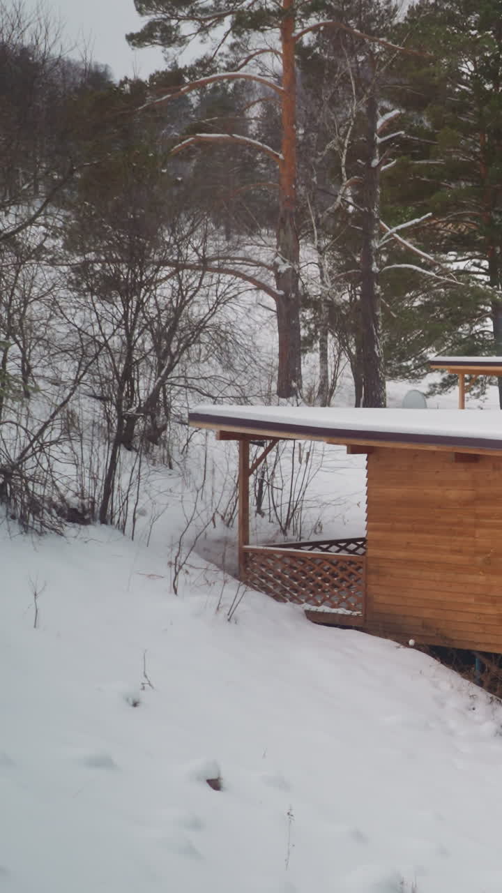 pequeña casa de madera con grandes ventanas construida en una ladera nevada entre árboles de coníferas. edificio para turistas en las tierras altas de gorny altai en un frío día de invierno
