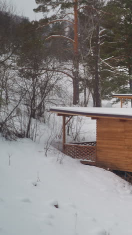 pequeña casa de madera con grandes ventanas construida en una ladera nevada entre árboles de coníferas. edificio para turistas en las tierras altas de gorny altai en un frío día de invierno