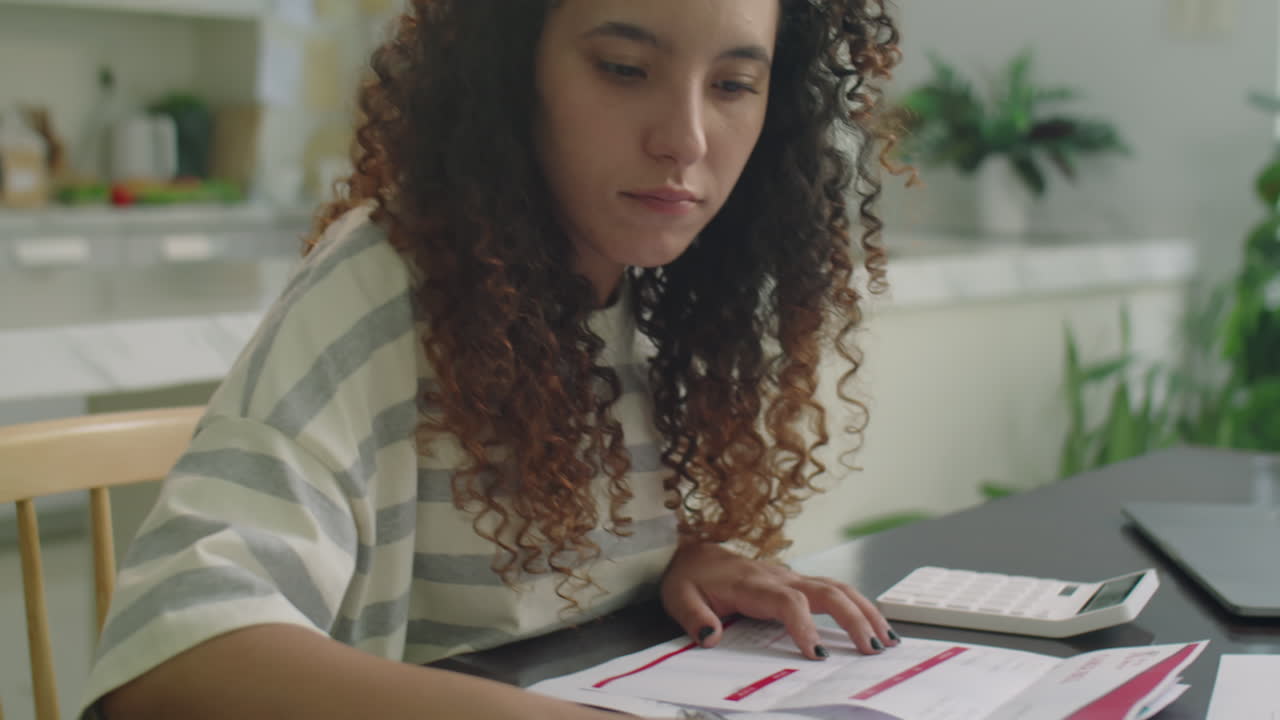 Girl Examining Bills and Using Calculator at Home