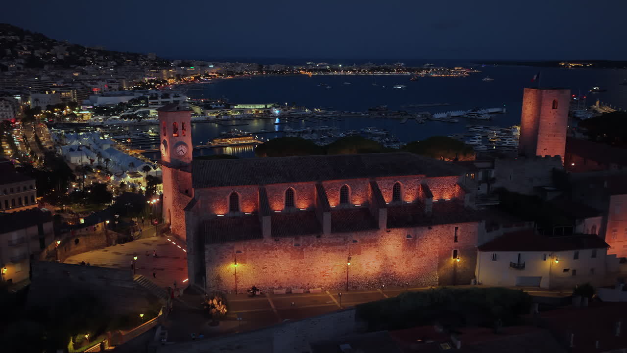 Vista aerea con drone del Vieux Port di Cannes e del quartiere medievale di Le Suquet, con yacht ormeggiati nel porto turistico e la chiesa di Notre-Dame de l'Espérance splendidamente illuminata