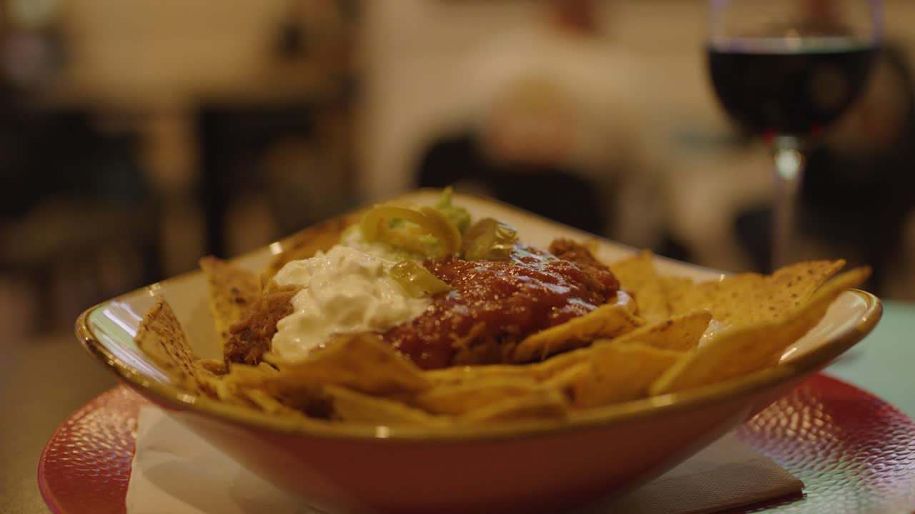 Corn chip with creamy nacho dip, salsa, jalapeños, and wine under warm bar lighting