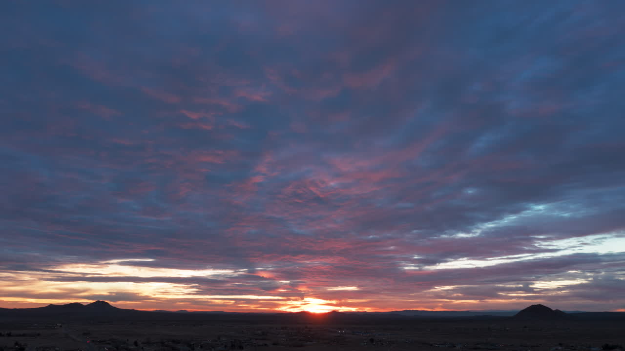 Una ola de nubes carmesí precede al amanecer dorado de un nuevo día en el desierto de Mojave - hiperlapse aéreo.