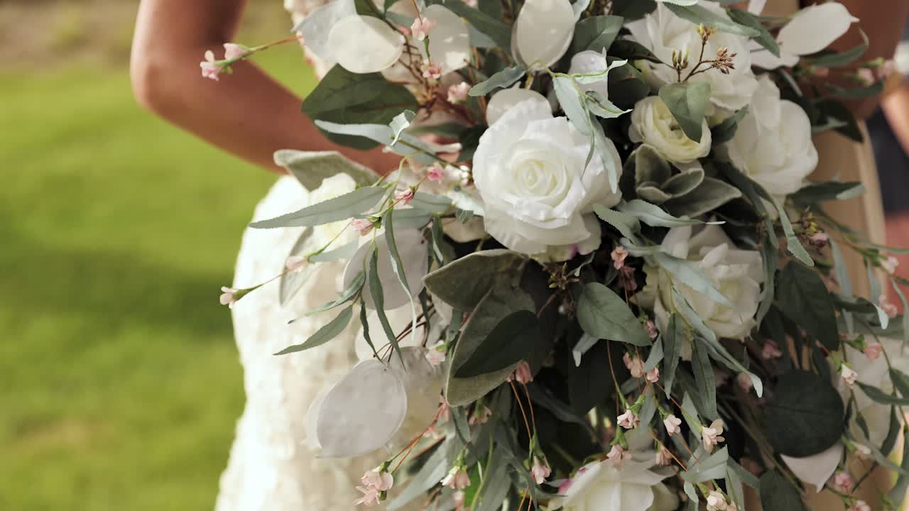 Close Up of Bride and in her Wedding Dress Holding Flower Bouquet in Her Hands Outdoors with White Roses and Greenery 1080p 60fps