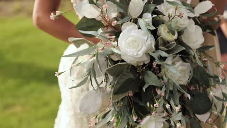 Cerca-De-La-Novia-Y-En-Su-Vestido-De-Novia-Sosteniendo-Un-Ramo-De-Flores-En-Sus-Manos-Al-Aire-Libre-Con-Rosas-Blancas-Y-Vegetación-1080p-60fps