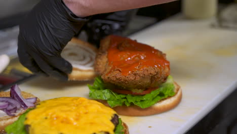 cook places top bun on buffalo chicken sandwich and cheeseburger, close up slow motion slide hd