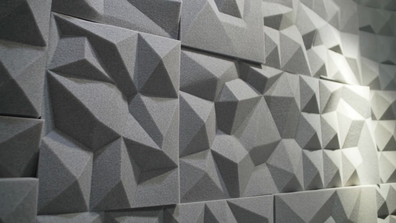 Close view of gray geometric wall panels with matte faceted surfaces, repeated polygon shapes, strong shadow play, and subtle depth for modern industrial interior backdrop, with abstract, geometric