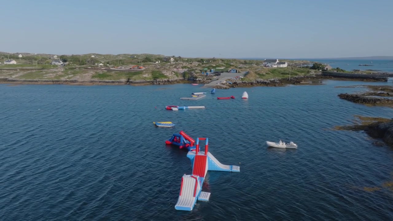 Des obstacles gonflables colorés de parc aquatique s'étendent sur un bras de mer calme près de bateaux et de rivages rocheux dans la région rurale de Lettermullan.