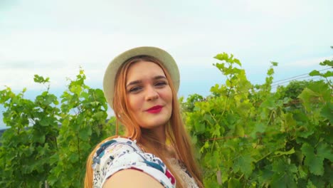 impresionantes imágenes en hd de una joven blanca caucásica con un sombrero de punto y lápiz labial rojo sosteniendo la cámara, sonriendo y posando entre los viñedos