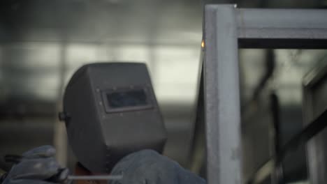 white caucasian man is welding metal frame with protective face mask