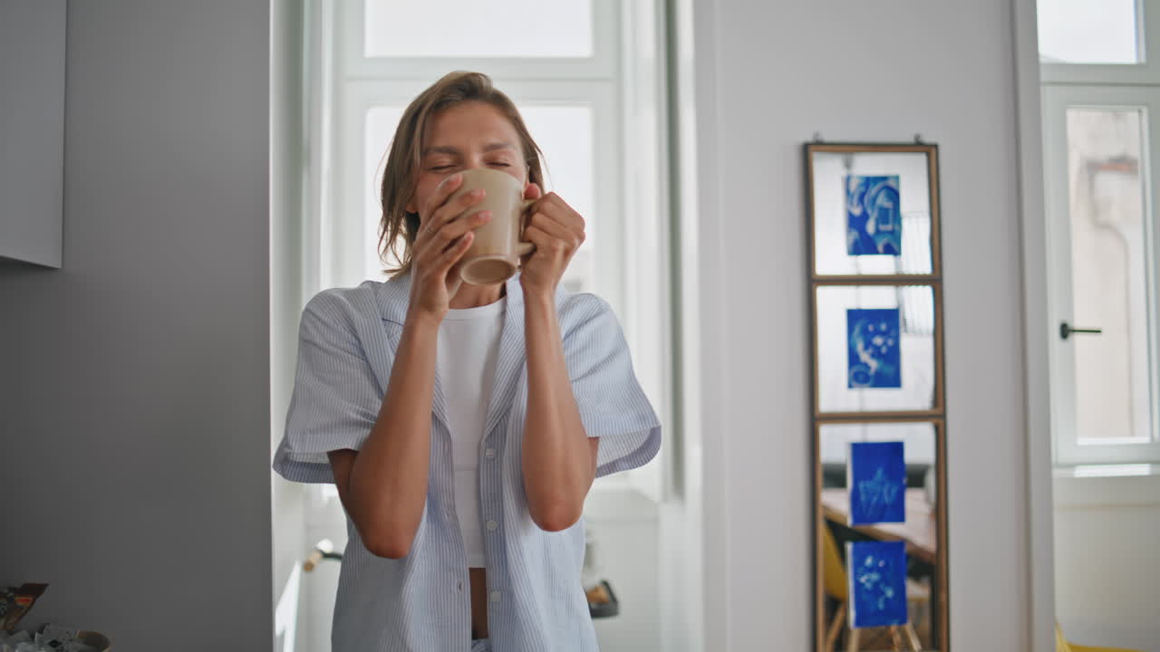 Donna che beve un caffè in cucina, provando beatitudine. Primo piano di una ragazza felice che sorseggia