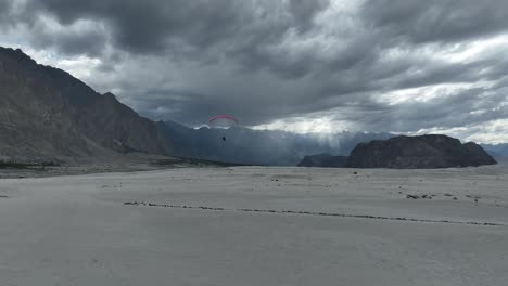 aerial view of paraglider soaring over sarfaranga desert with dramatic overcast clouds