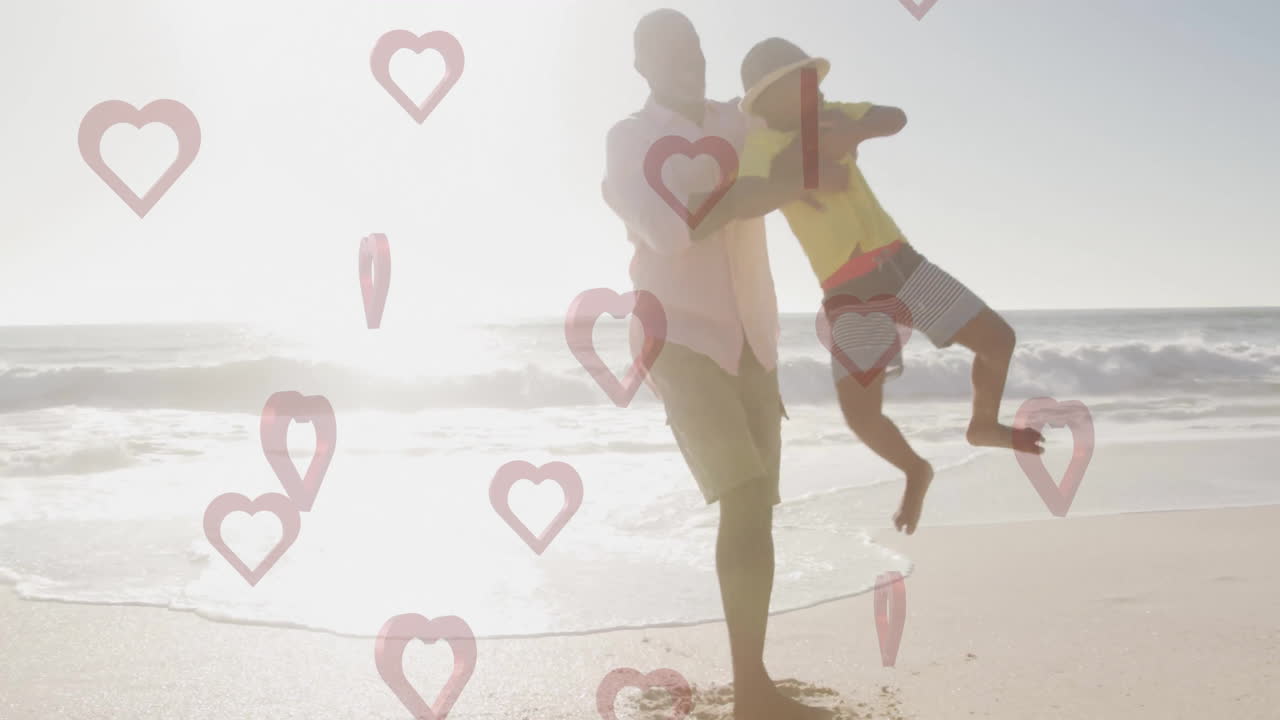 Father playing with child on beach, hearts animation over sunny background