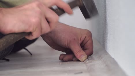 man using a hammer to nail laminate batten