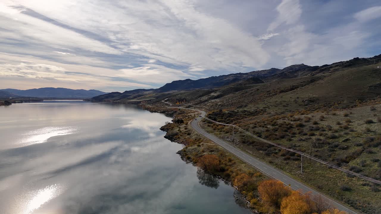 Aerial view of Lake Dunstan with surrounding landscape, showcasing roads and autumn foliage under a dramatic sky