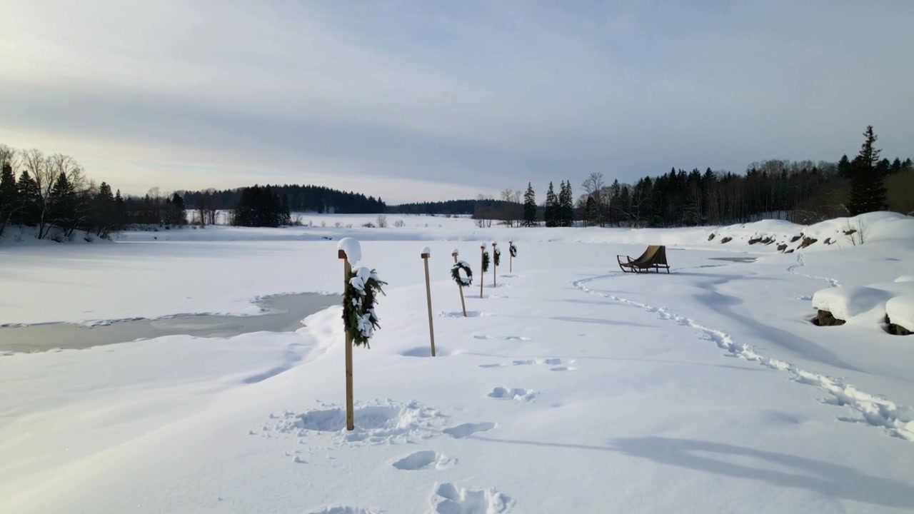 Panning camera showing row of wooden posts with wreaths leading into frozen shore, footprints