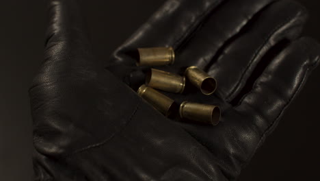 mano con guante de cuero negro que se abre y revela casquillos de bala de 9 mm