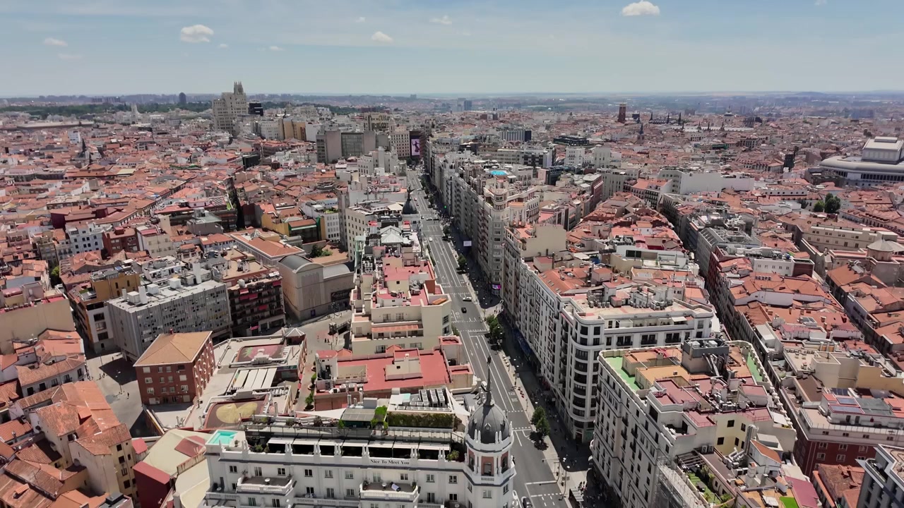 Ampie riprese aeree dell'iconica Gran Via di Madrid sotto l'intensa luce solare estiva, che evidenziano la classica architettura spagnola, i tetti illuminati dal sole e le strade animate da una prospettiva mozzafiato di un drone