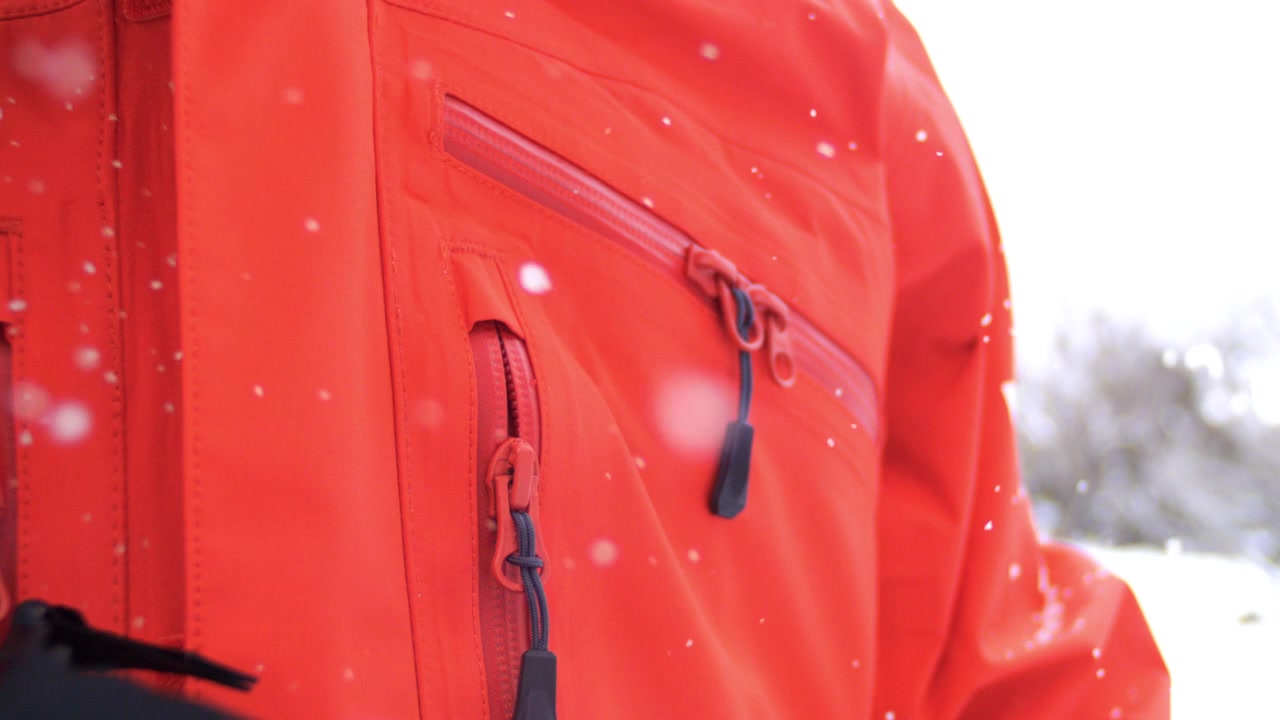 Person adjusts heavy-duty zipper on red winter jacket using the pull tab in snowy weather