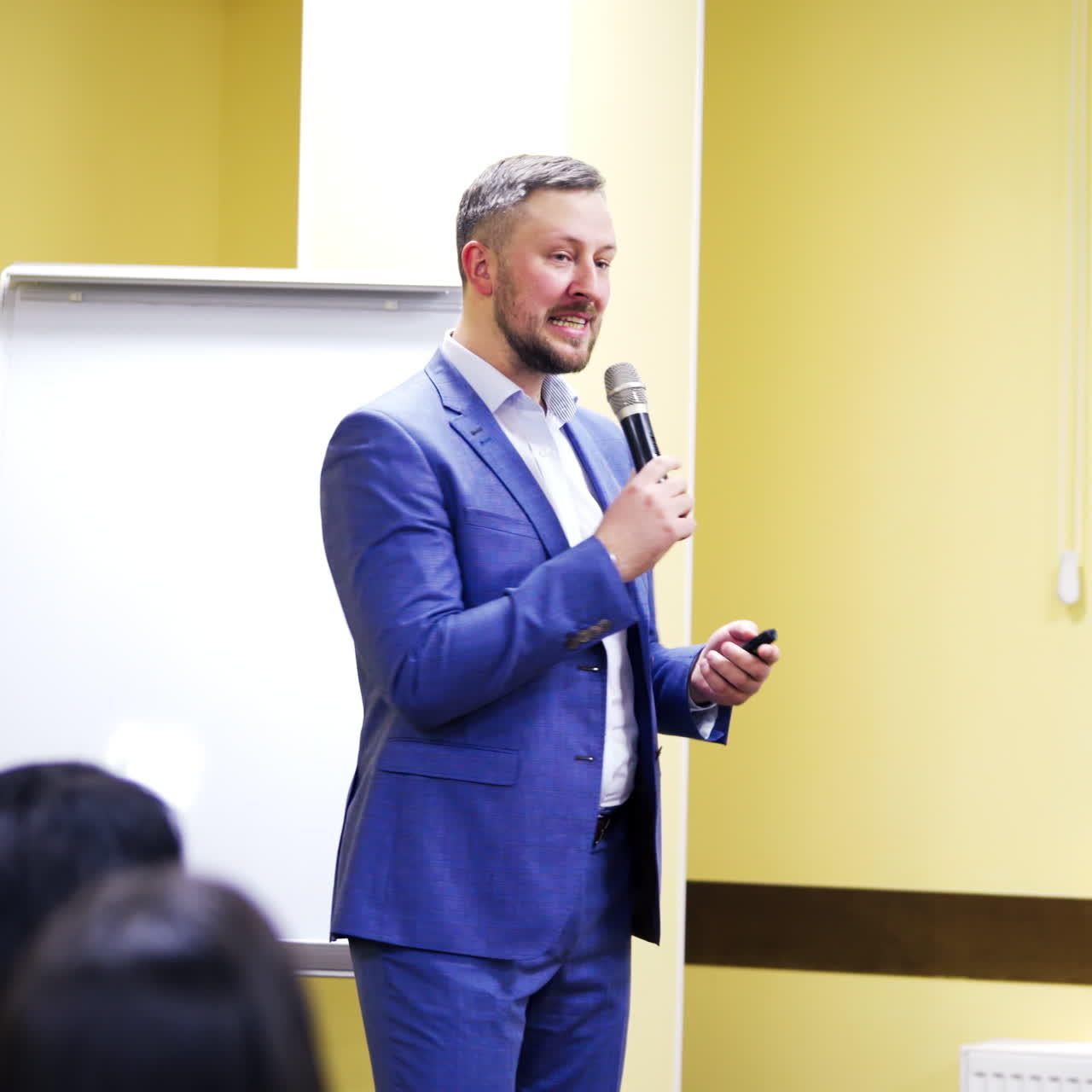 Businessman in elegant suit explaining the lecture in the conference room. Handsome male speaker with the microphone conducts speech with a smile on his face.