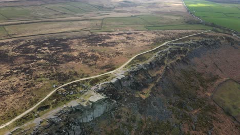 Aerial-footage-over-dramatic-rock-formation-Stanage-Edge-in-the-Peak-District-with-a-single-person-hiking-a-long-trail-in-the-distance