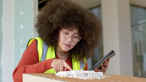 casual biracial female architect with tablet looking at 3d model in office, slow motion, copy space
