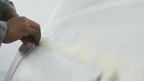 african american male car mechanic cutting a protective cover on a car with a razor blade