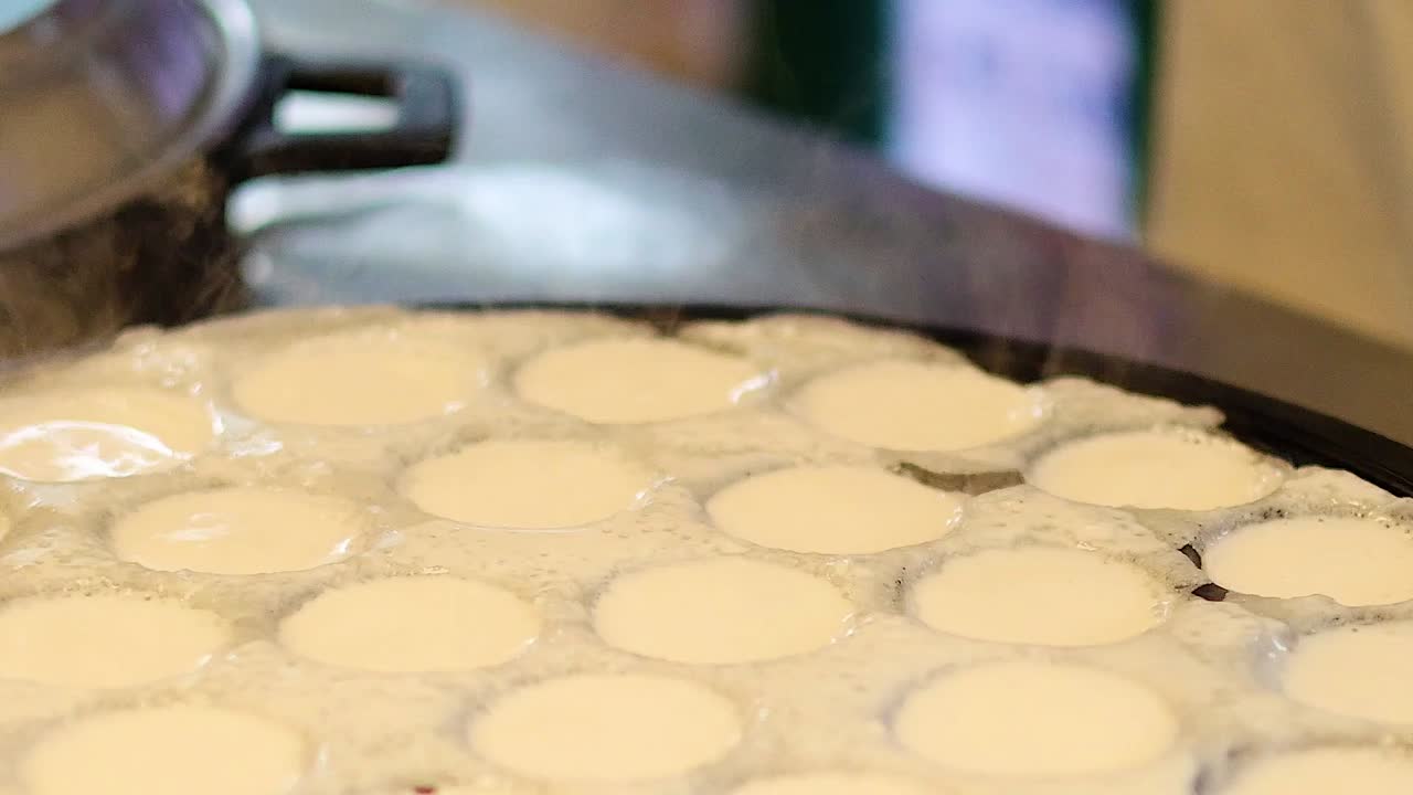Traditional coconut batter simmers and sets inside round molds of a hot cast iron pan