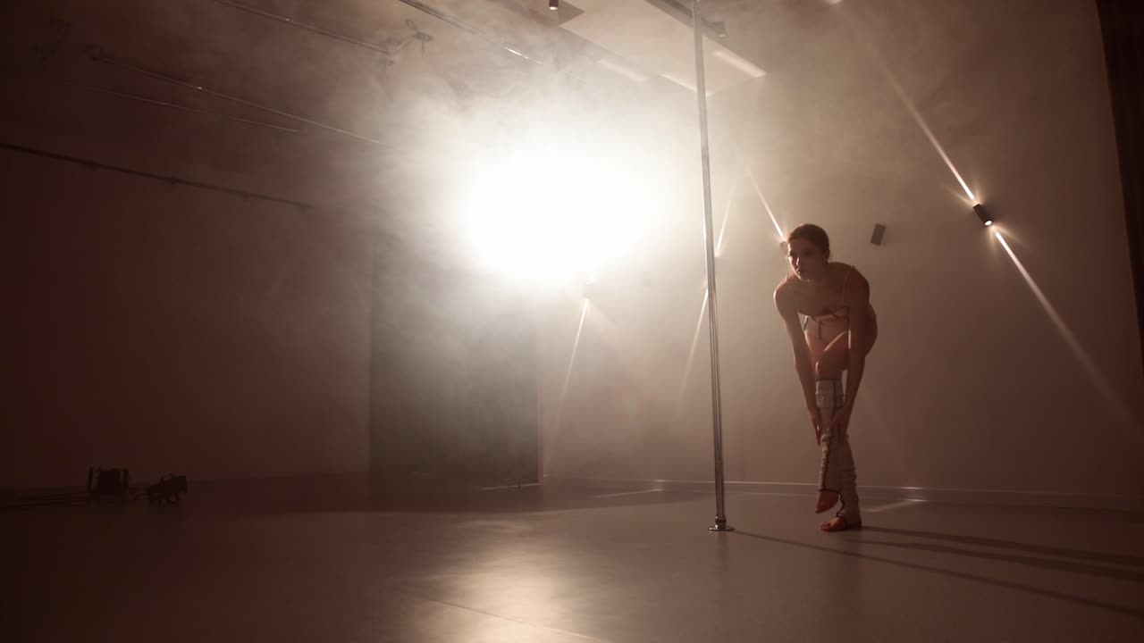 Young pole dancer adjusting socks in an indoor smoky studio