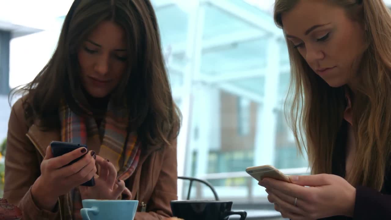 Pretty friends enjoying coffee in cafe using phones