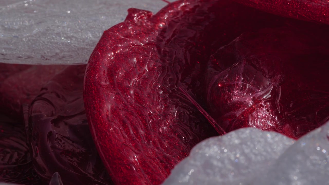 Extreme close up of glossy melted red plastic mass being extruded and processed inside recycling machinery