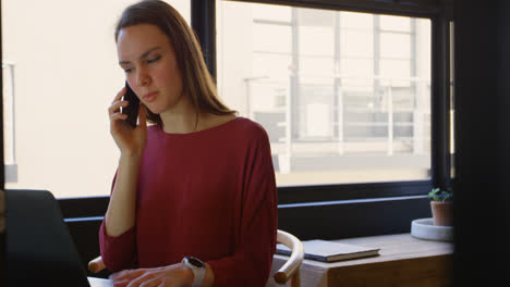 Front-view-of-young-caucasian-businesswoman-with-laptop-talking-on-mobile-phone-in-modern-office-4k