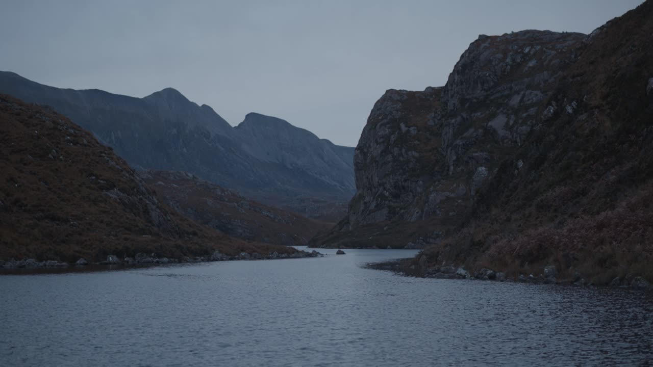Loch na Thull in the Scottish Highlands. Rugged cliffs and mountain peaks rise above the water, reflecting a dramatic and remote wilderness landscape with a cinematic atmosphere