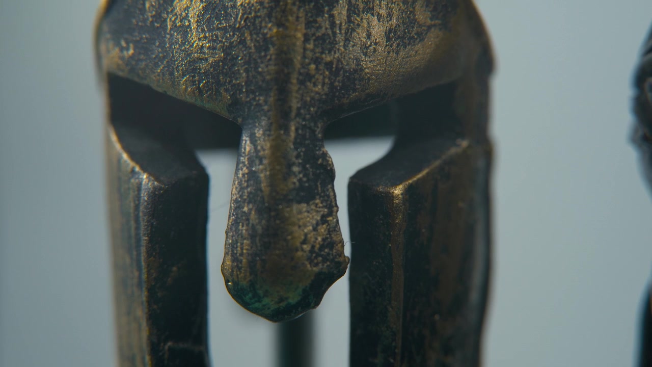 En kreativ makrobild i närbild av en spartansk design, antik krigarhjälm i metallbrons, glödande texturerade ansiktsmaskformer, studiobelysning, mjuk 4K cinematiskt video, Slow Motion, uppåtlutande rörelse.