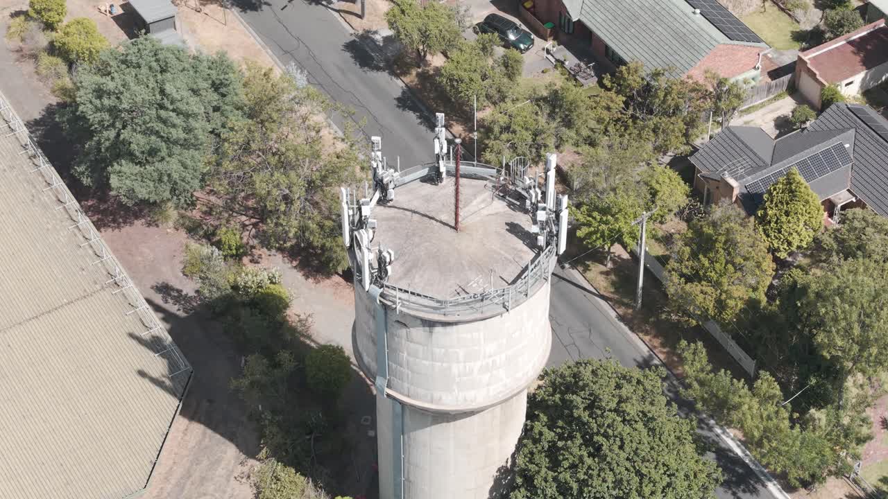 Drohnenaufnahme zeigt einen Wasserturm in einem australischen Vorort. Umgeben von Grünflächen und Dächern, hebt diese Aufnahme aus hoher Perspektive die urbane Architektur unter der Sonne hervor.